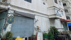 Un edificio de varios pisos con una planta baja comercial, que presenta una tienda cerrada con persiana metálica y un cartel.