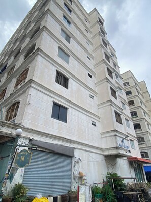 Un edificio de varios pisos con una planta baja comercial, que presenta una tienda cerrada con persiana metálica y un cartel.