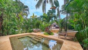 A pool area with steps leading into the water, surrounded by lush tropical vegetation and wicker furniture. - Elegant 2BR Jungle Sanctuary Private Terrace Pool Access (Higuera Blanca)