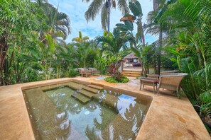 A pool area with steps leading into the water, surrounded by lush tropical vegetation and wicker furniture. - Elegant 2BR Jungle Sanctuary Private Terrace Pool Access (Higuera Blanca)