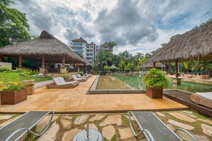 A resort pool area with lounge chairs, thatched umbrellas, and a large pool. - Elegant 2BR Jungle Sanctuary Private Terrace Pool Access (Higuera Blanca)