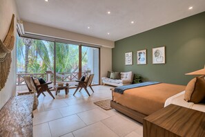 A modern bedroom with a large bed, a sofa, a dining table, and a balcony with a view of trees. - Elegant 2BR Jungle Sanctuary Private Terrace Pool Access (Higuera Blanca)