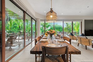 A dining area with a large table set for six, surrounded by chairs, with a hanging light fixture above. - Elegant 2BR Jungle Sanctuary Private Terrace Pool Access (Higuera Blanca)
