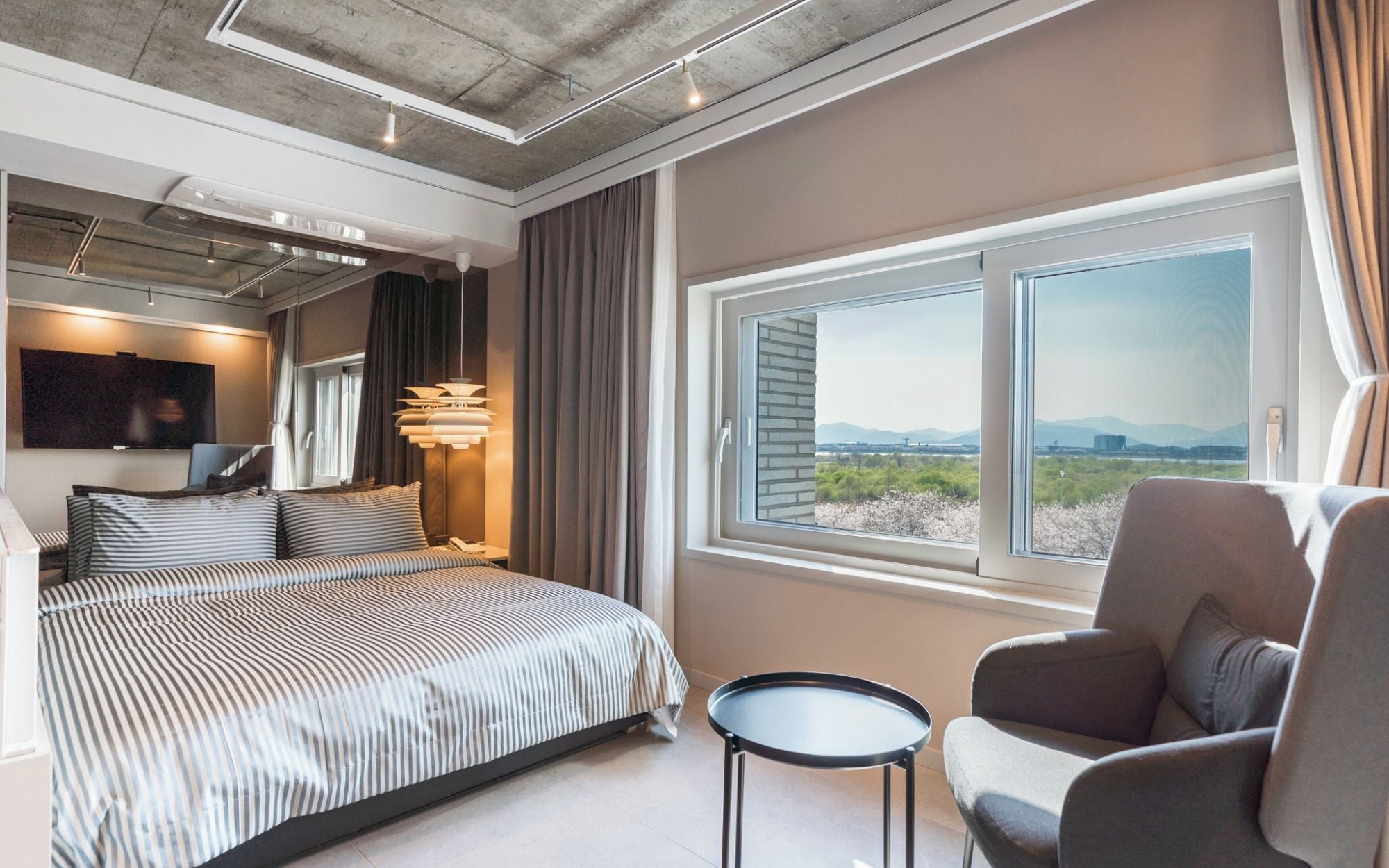 A modern hotel room with a large bed, a seating area, a TV, and a window with a view.