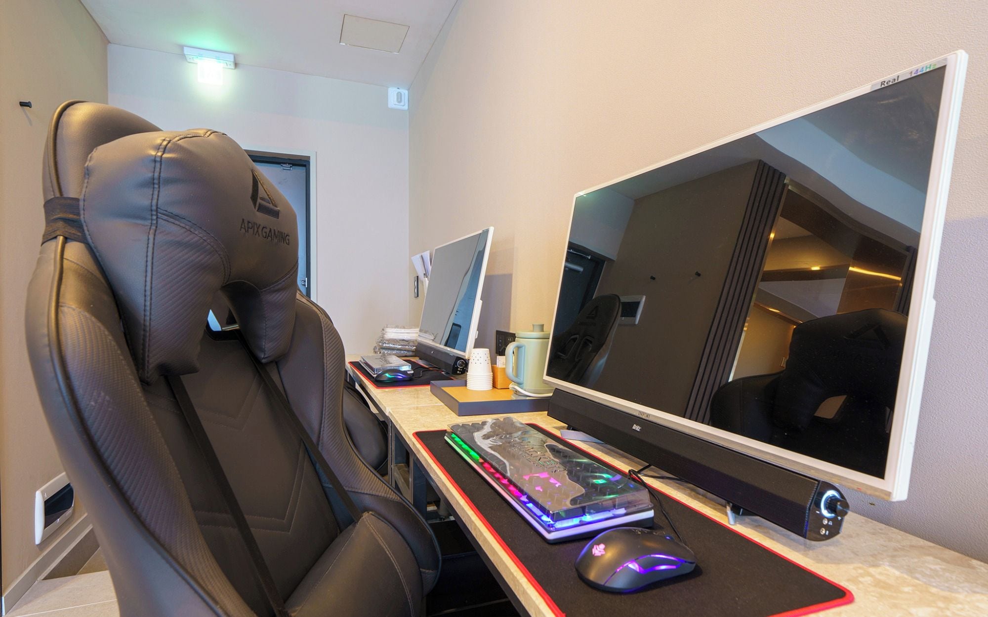 Una sedia da gaming con l'etichetta 'APIX GAMING' e una scrivania con computer, tastiera, mouse e monitor.