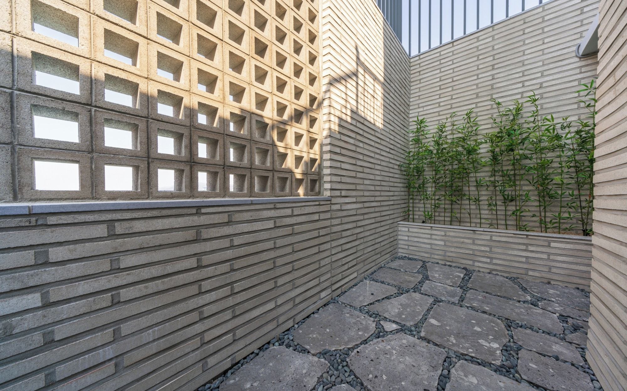 Un patio con un muro decorado, un jardín de bambú y un sendero de piedra.