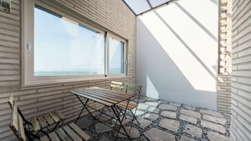 A balcony with a table and benches, a large window with a view, and a patterned stone floor.