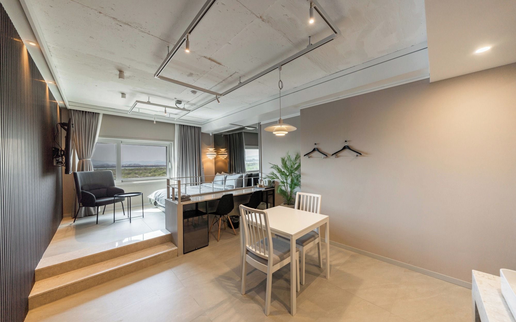 A modern hotel room with a dining area, a staircase leading to an outdoor terrace, and a view of the landscape.