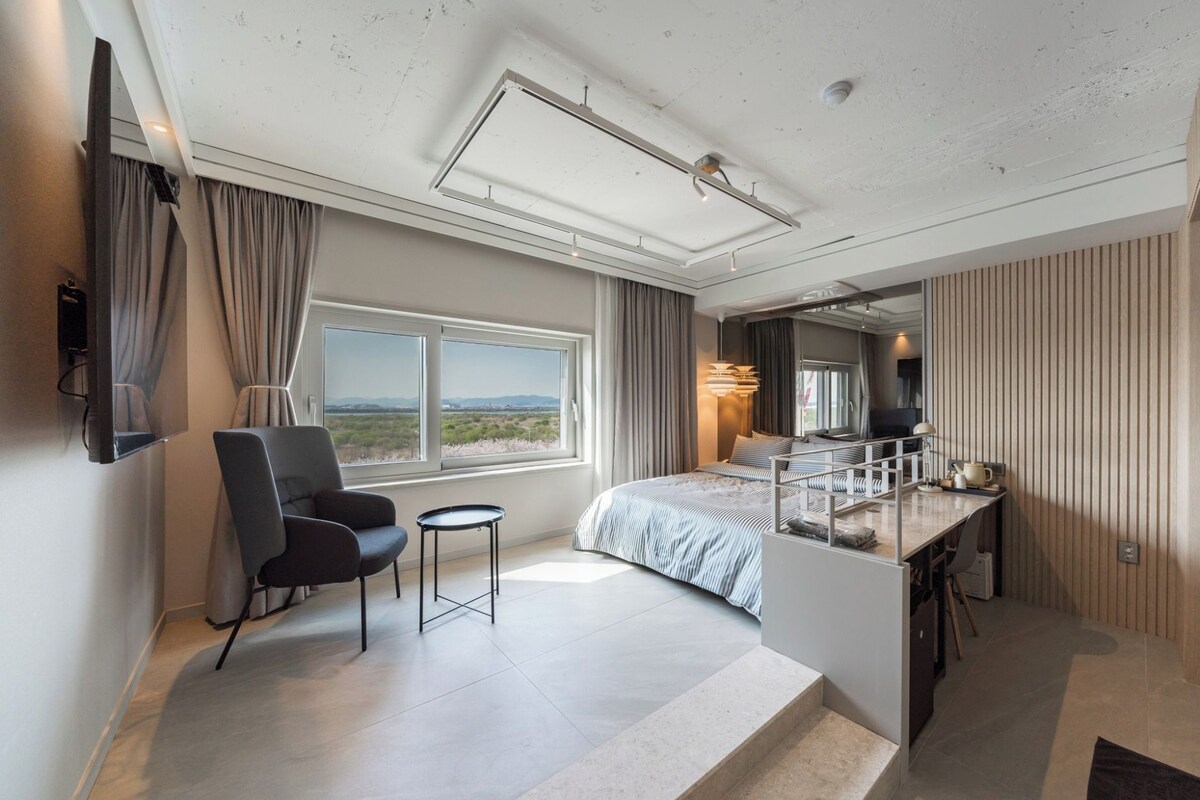 Et moderne hotelværelse med seng, skrivebord, stol, fjernsyn og et stort vindue med udsigt.
