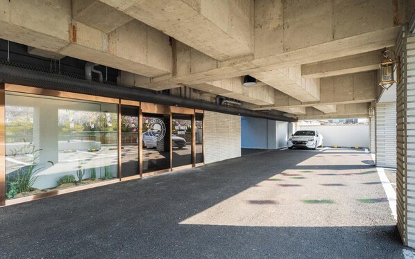 A hotel entrance with a glass facade, a car parked inside, and a concrete ceiling structure. - Busan Sasang Mr. Brick Hotel (Busan)
