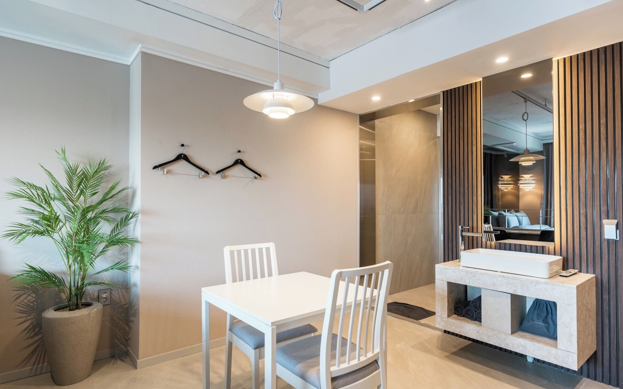 A modern dining area with a white table and chairs, a hanging light fixture, and a potted plant.