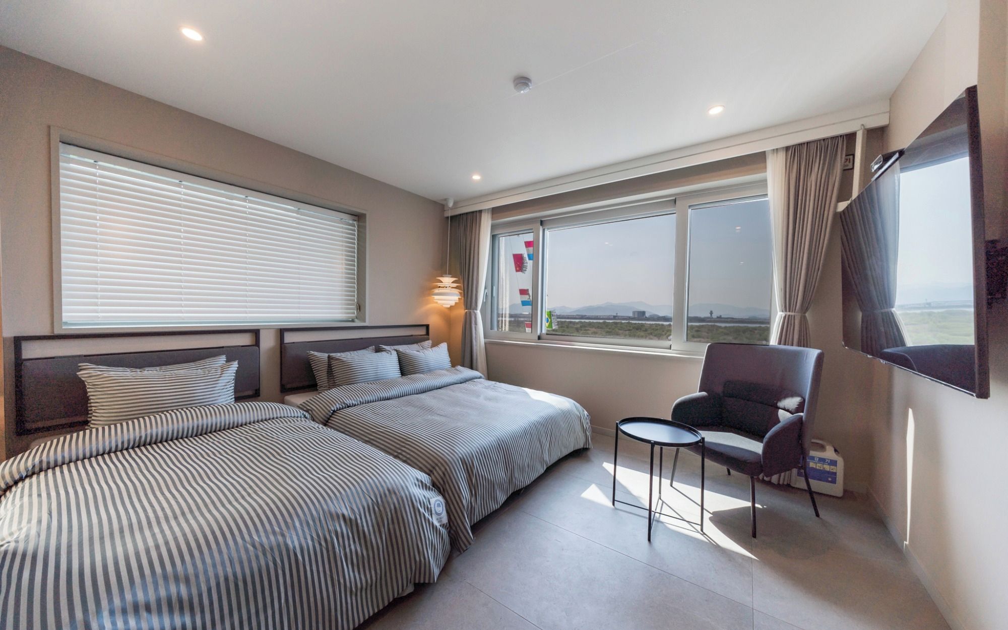 Une chambre d’hôtel avec deux lits, une chaise, un téléviseur et une fenêtre donnant sur un paysage agréable.