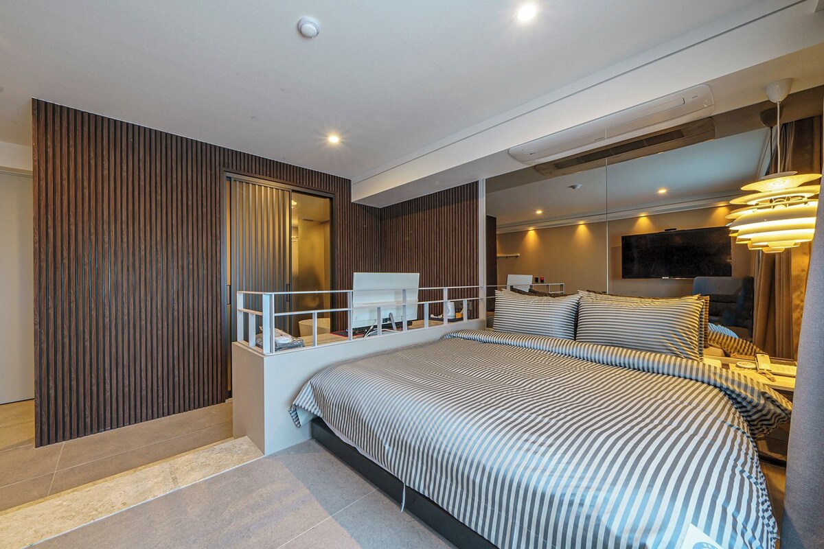 Ein modernes Schlafzimmer mit einem großen Bett, einer kleinen Sitzecke, einem Fernseher und einem Balkon.