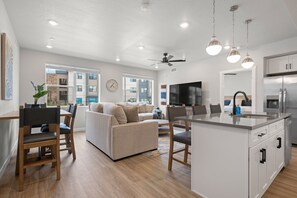 Een moderne woonkamer met een bank, eettafel en keuken voorzien van een koelkast en gootsteen.