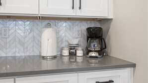 Una cucina con mobili bianchi, una macchina da caffè e tre barattoli etichettati con il loro contenuto.