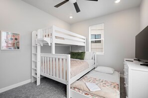 A bunk bed room with a ceiling fan, a window with blinds, a television on a stand, and a framed picture on the wall. - Splash Zone | A Family Favorite near Zion (Hurricane)