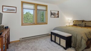 A bedroom with a bed, a bench, a TV, and a window with blinds. - The Back Nine | Golf, Mount Snow, & Vermont Escape (Wilmington)