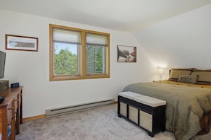 Ein Schlafzimmer mit einem Bett, einer Bank, einem Fernseher und einem Fenster mit Jalousien.