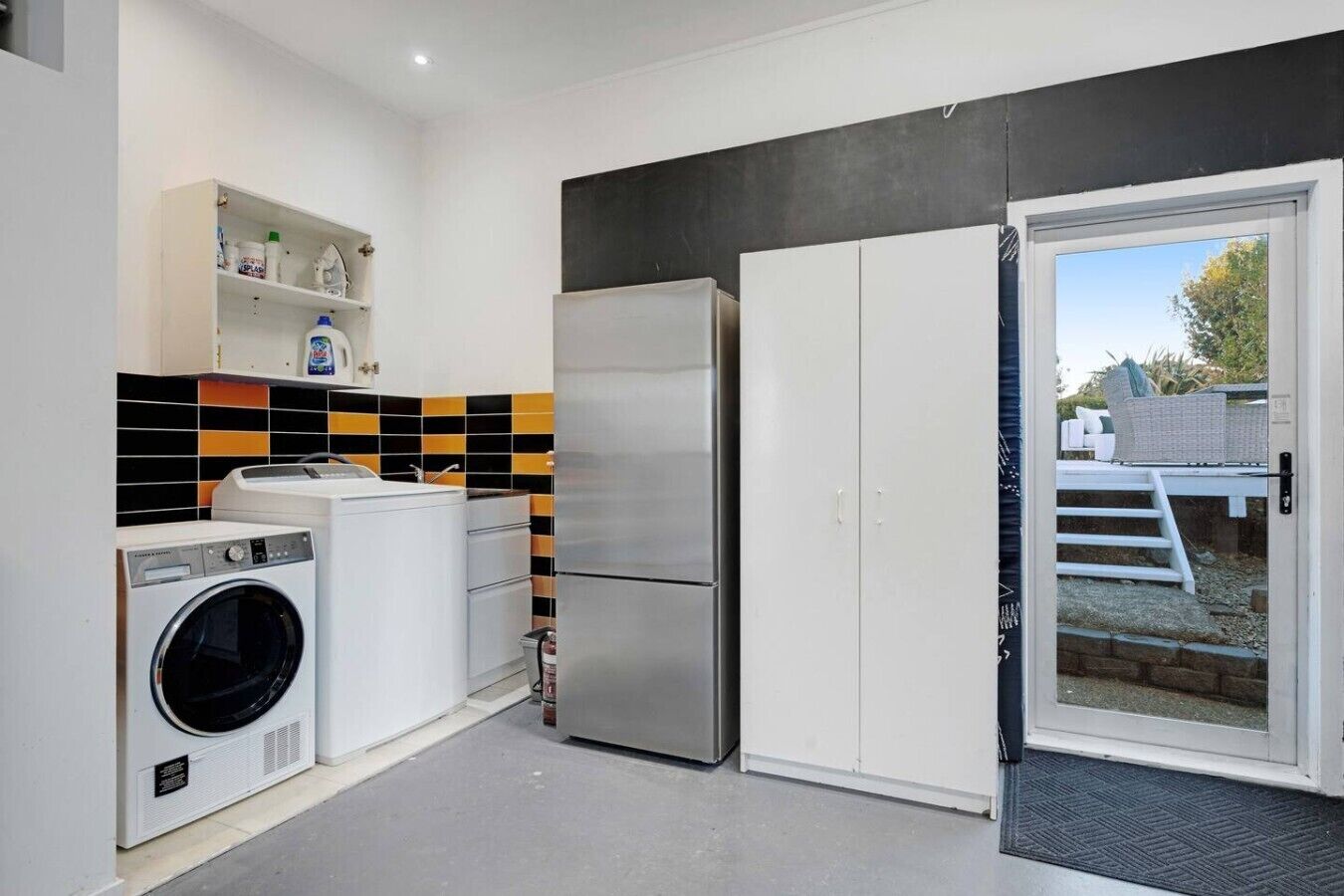 Eine kompakte Küche mit Waschmaschine, Kühlschrank und integriertem Regal für Reinigungsmittel.