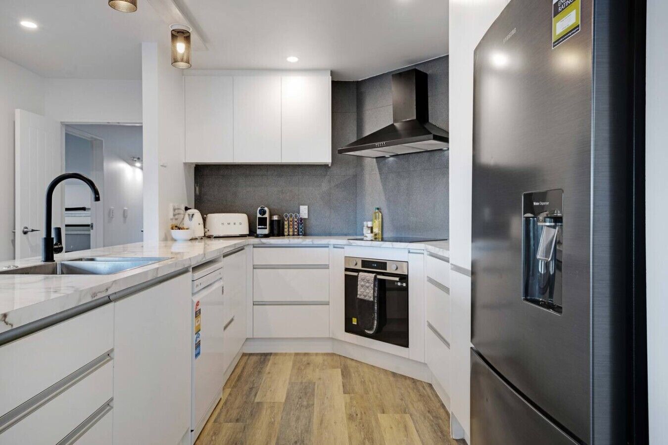 Eine moderne Küche mit weißen Schränken, einem Edelstahl-Kühlschrank, einem eingebauten Backofen und einer Arbeitsplatte mit einem Toaster und weiteren Geräten.
