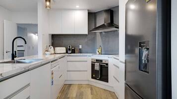 Eine moderne Küche mit weißen Schränken, einem Edelstahl-Kühlschrank, einem eingebauten Backofen und einer Arbeitsplatte mit einem Toaster und weiteren Geräten.