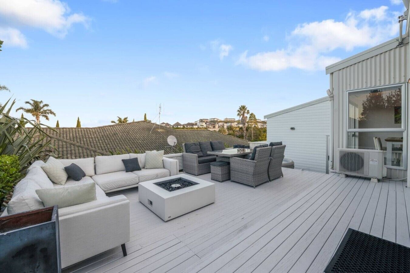 Eine Dachterrasse mit Gartenmöbeln, darunter Sofas und ein Couchtisch, und ein modernes Gebäude im Hintergrund.