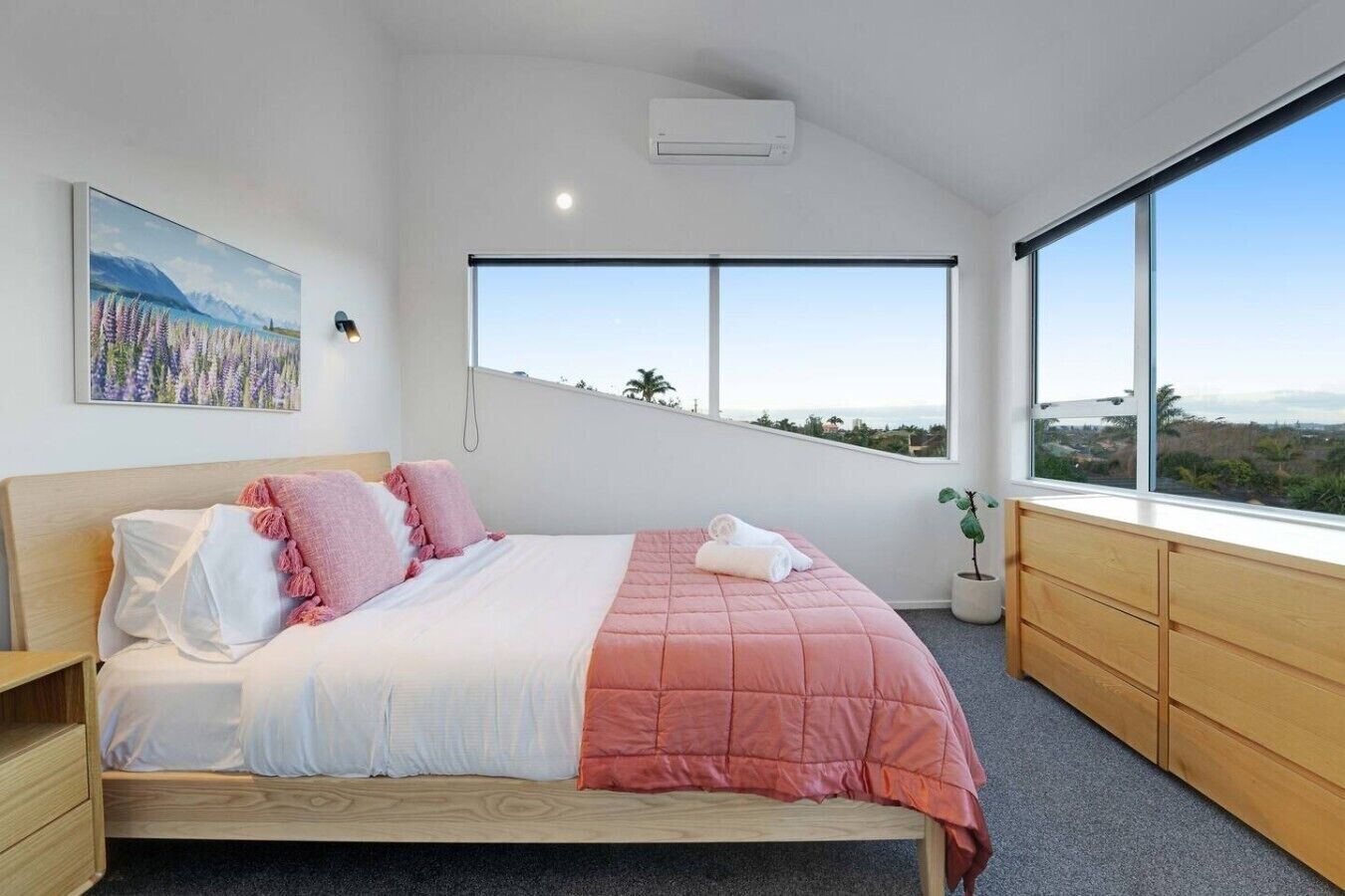 Ein modernes Schlafzimmer mit einem großen Bett, Blick ins Freie und einem Gemälde an der Wand.