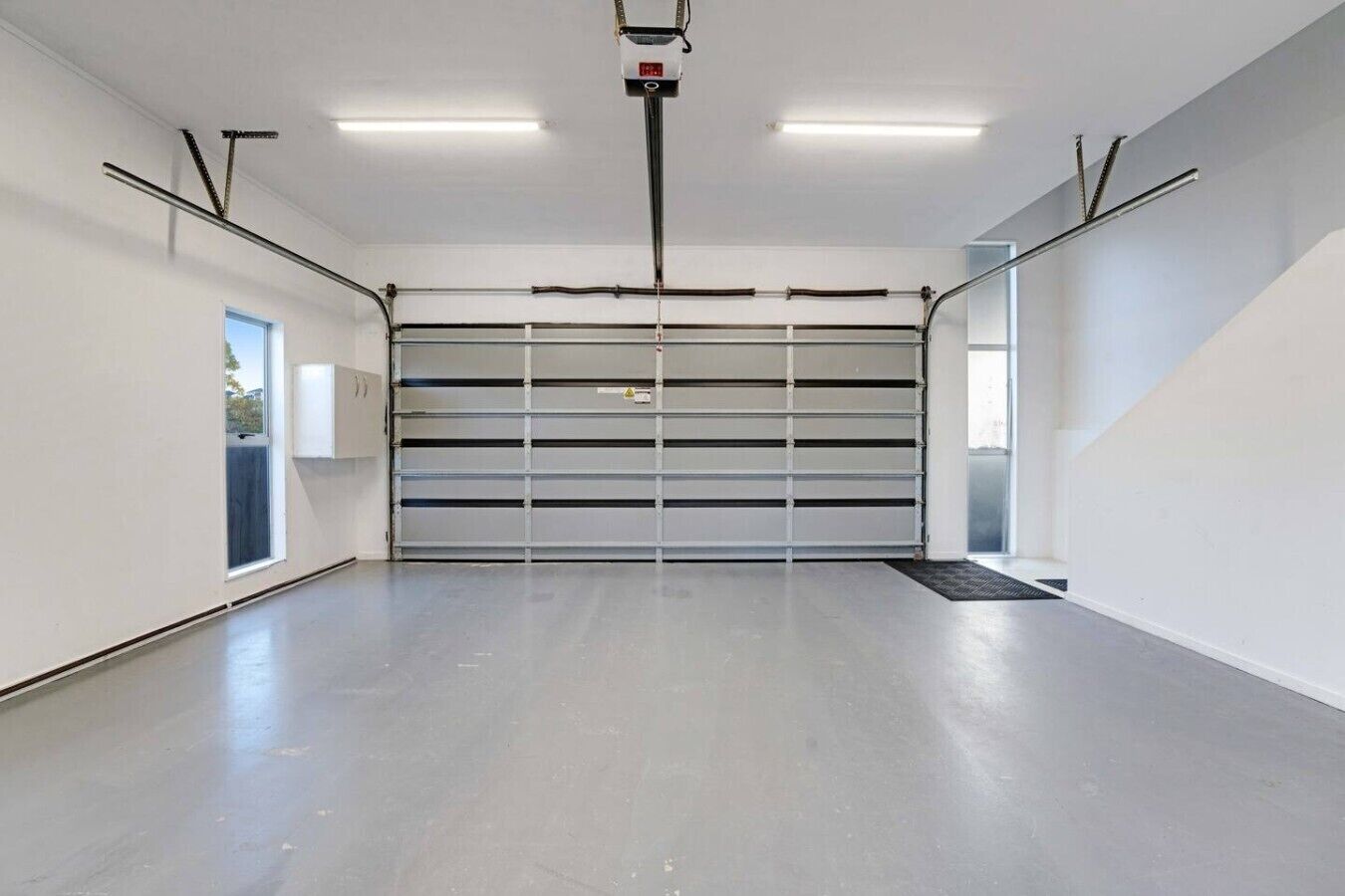 A spacious, empty garage with a large, closed garage door, fluorescent lighting, and a clean, concrete floor.