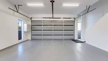 A spacious, empty garage with a large, closed garage door, fluorescent lighting, and a clean, concrete floor.