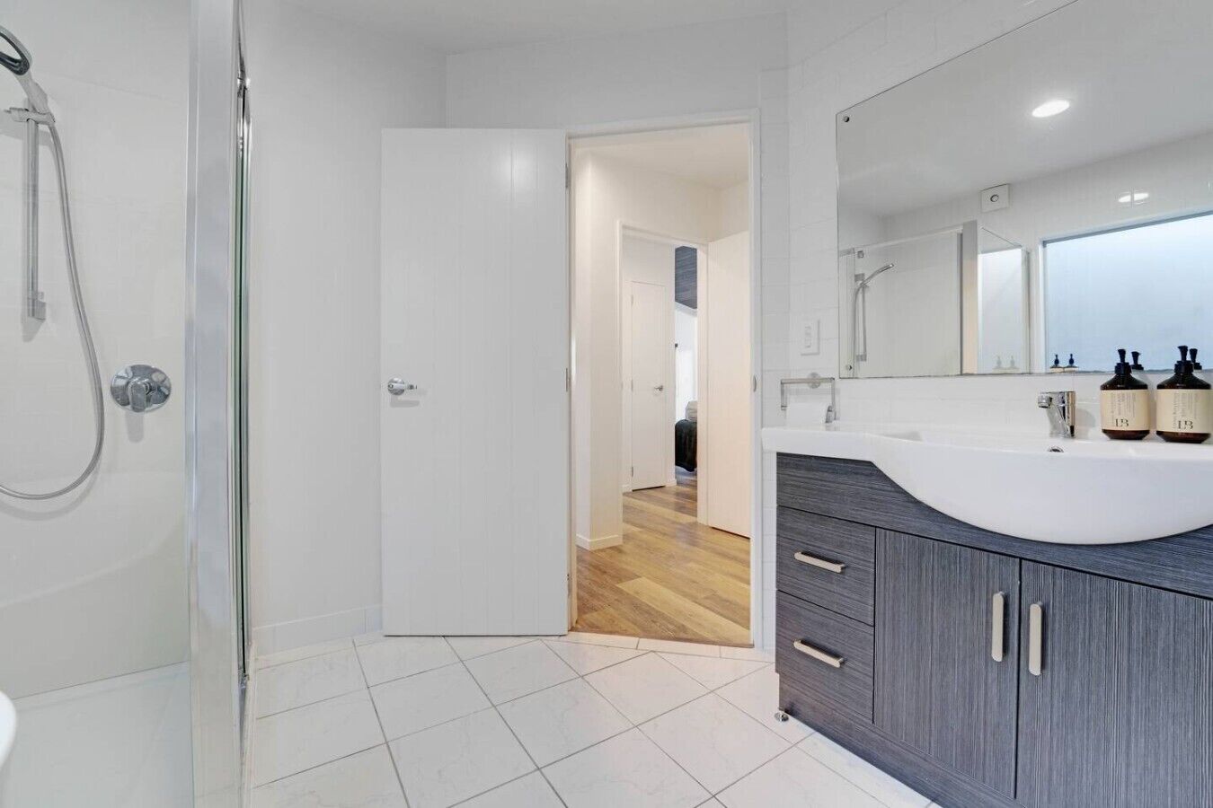 A modern bathroom with a shower, a sink with a mirror, and a door leading to another room.