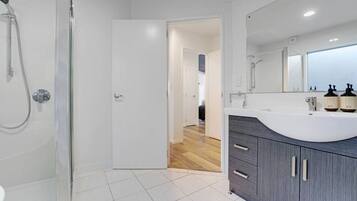 A modern bathroom with a shower, a sink with a mirror, and a door leading to another room.