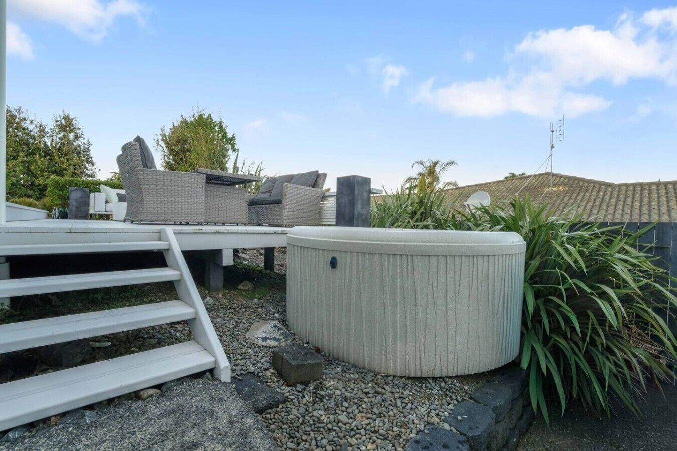 Eine Terrassenfläche mit Gartenmöbeln, einem Whirlpool und einer Treppe zu einer erhöhten Holzterrasse.