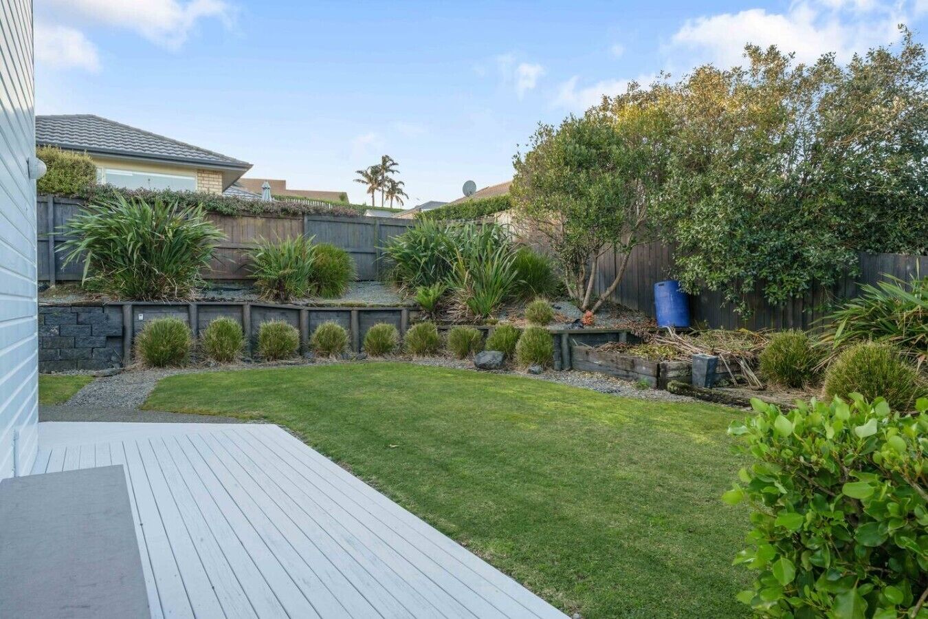 Un jardin avec une terrasse en bois, une pelouse bien entretenue et divers arbustes et plantes.