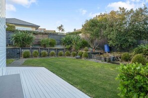 A backyard with a wooden deck, a well-maintained lawn, and various shrubs and plants.