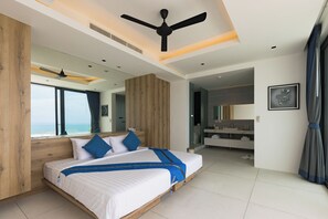 A modern bedroom with a large bed, a ceiling fan, a bathroom with a vanity, and a view of the sea. - Blue View Luxe by Sublime Samui Villas (Koh Samui)