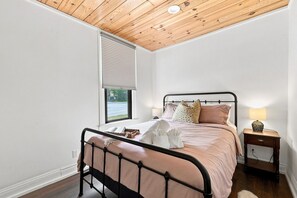 Ein Schlafzimmer mit einem Bett, einem Nachttisch, einem Fenster mit Jalousien und einer Holzbalkendecke.
