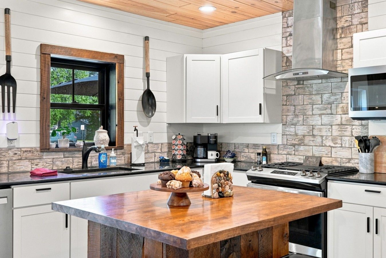 A modern kitchen with white cabinetry, a wooden island, and a stone backsplash.