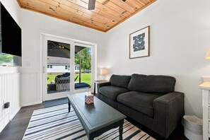 Una sala de estar con sofá, una mesa de centro, televisor y puerta corrediza de vidrio que da a una zona de estar exterior.
