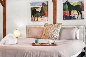 Una habitación de hotel con una cama, una bandeja con una taza y una taza, una lámpara y dos cuadros en la pared.