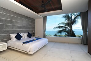 Une chambre moderne avec un grand lit, un ventilateur de plafond et une vue sur l’océan.