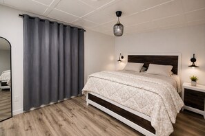 A bedroom with a bed, a nightstand, a potted plant, a wall-mounted lamp, and a large mirror. - Zen on the Lake Spa | Mission, BC (Mission)