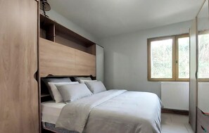 A bedroom with a bed, built-in storage, a window, and a radiator.