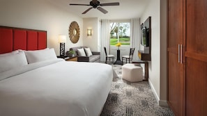 Ein Hotelzimmer mit einem großen Bett, einem Sofa, einem kleinen Tisch mit Stühlen, einem Deckenventilator und einem Fernseher.