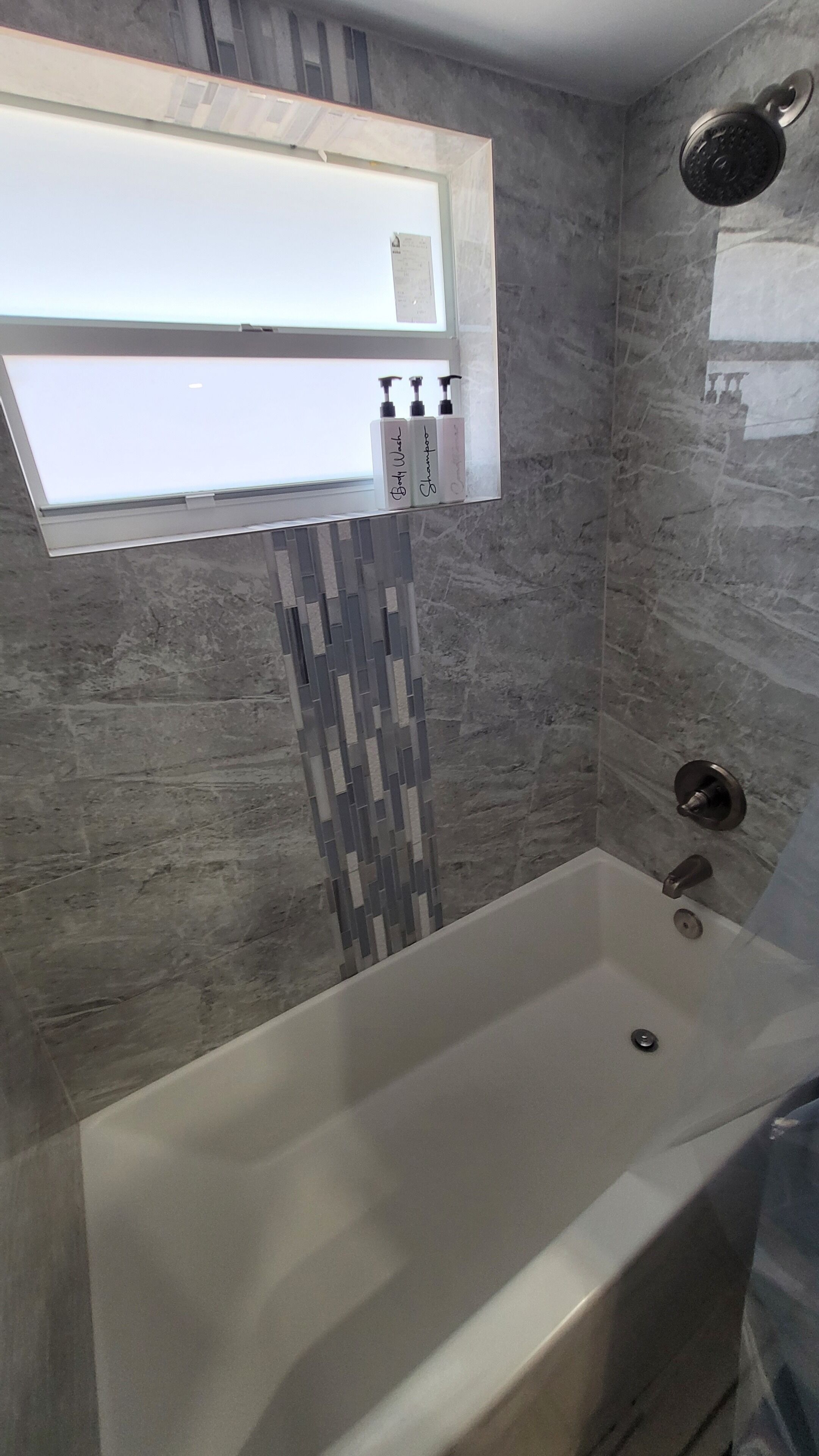 A bathroom with a bathtub, a showerhead, and a mirror reflecting a window.
