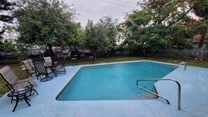 Une piscine rectangulaire avec un escalier en métal, entourée d’une clôture et d’arbres.