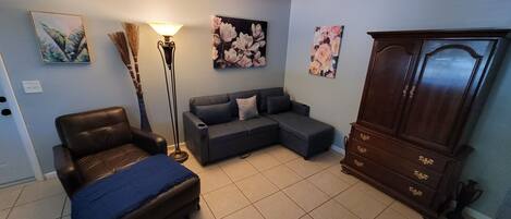 Un salon comprenant un canapé, un fauteuil, une lampe sur pied et un meuble.
