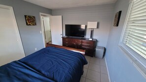 A bedroom with a bed, a dresser, a television, and a window with blinds. - You'll love it here (Palm Beach Gardens)