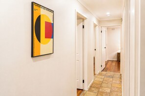 Ein Flur mit einem geometrischen Kunstwerk an der Wand, weißen Türen und einem gemusterten Boden.