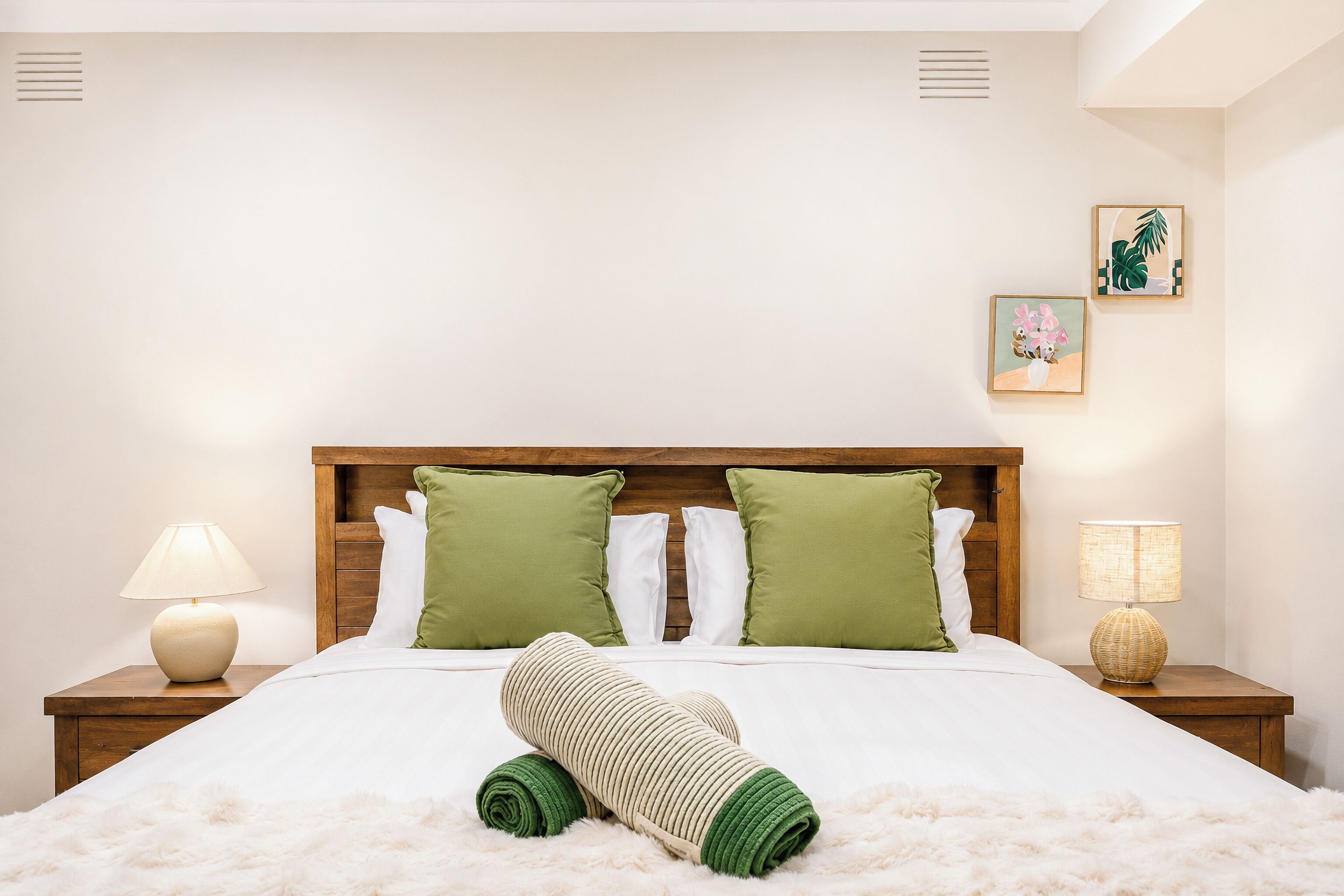 Habitació d'hotel amb un llit gran, dos coixins, una làmpada de nit, un quadre penjat a la paret i una catifes blanca i esponjosa.