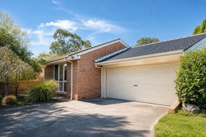 A residential property with a garage, a brick house, and a well-maintained lawn. - Wantirna 4BR Family Home | Space for Longer Stays (Wantirna South)